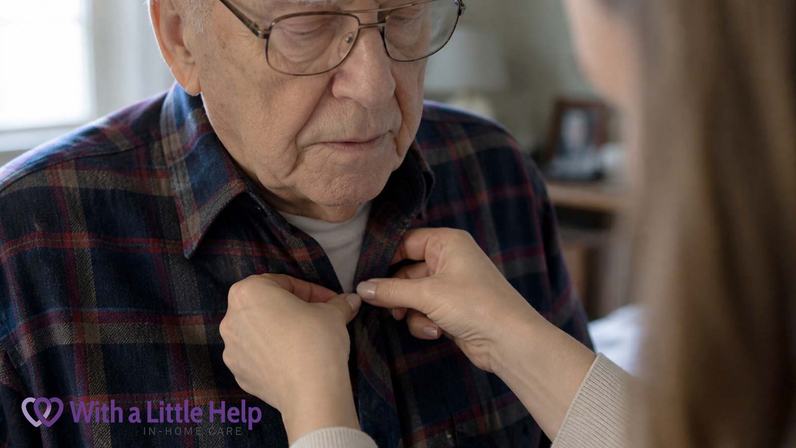 Caregiver helping elderly man button flannel shirt during daily care at home